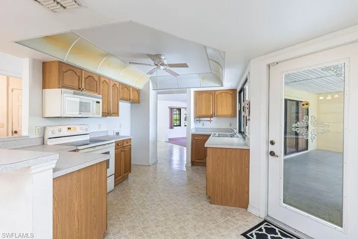Kitchen with white appliances, brown cabinets, light countertops, and a ceiling fan