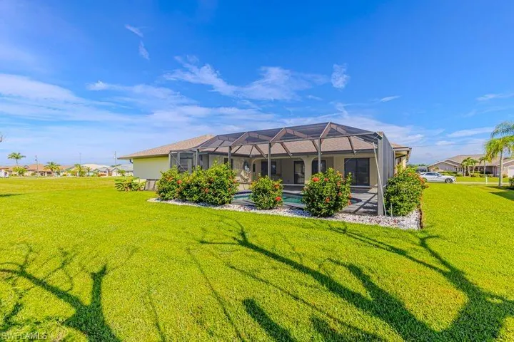 Rear view of house with a sunroom, glass enclosure, a lawn, a pool, and stucco siding