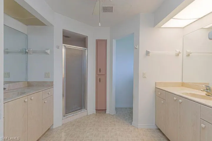 Full bath with two vanities, a shower stall, and ceiling fan