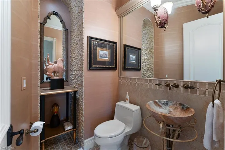 Bathroom with tile walls, crown molding, toilet, and sink