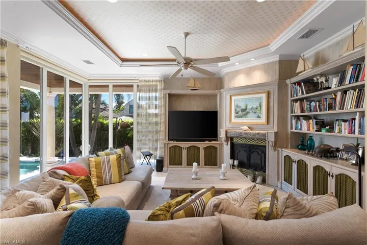 Living room featuring crown molding, built in features, a tray ceiling, and ceiling fan