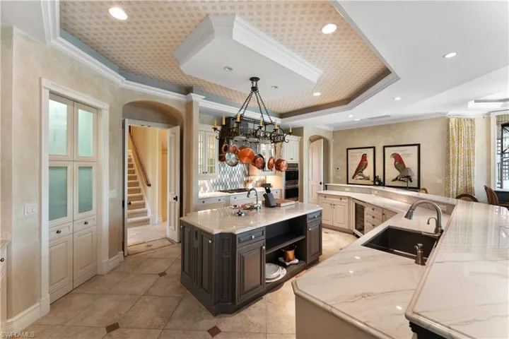 Kitchen featuring a large island, light stone counters, a raised ceiling, sink, and decorative light fixtures