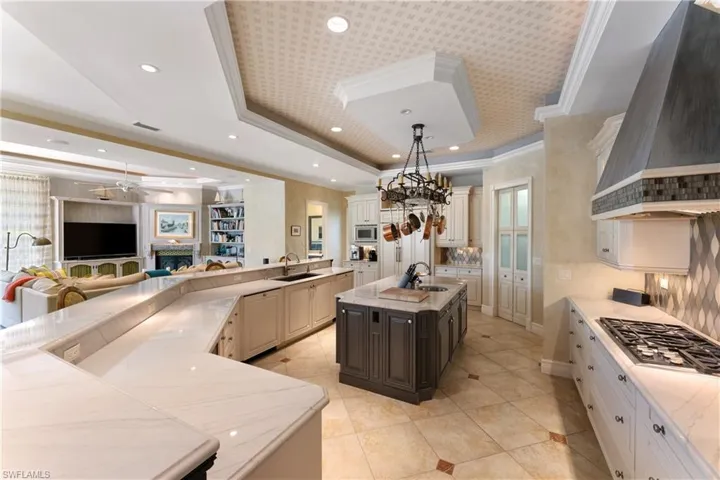 Kitchen with appliances with stainless steel finishes, sink, pendant lighting, custom range hood, and a center island with sink