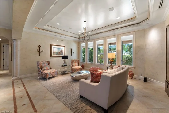 Living room featuring ornamental molding, decorative columns, a notable chandelier, and a raised ceiling
