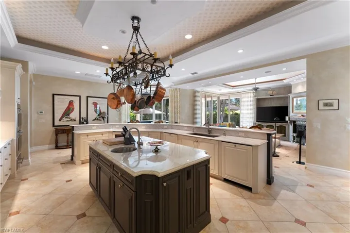 Kitchen featuring a center island with sink, sink, crown molding, a raised ceiling, and light stone counters
