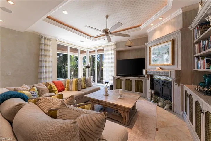 Tiled living room featuring crown molding, built in features, a tray ceiling, and ceiling fan