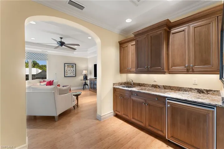 Bar featuring crown molding, sink, light wood-type flooring, ceiling fan, and light stone counters