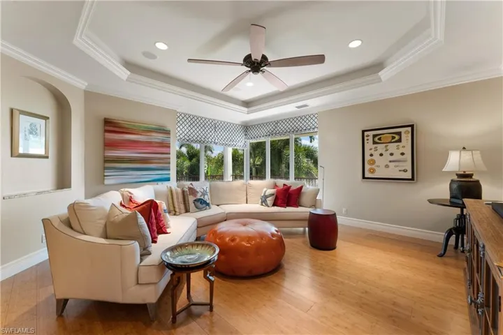 Living room with ornamental molding, ceiling fan, light hardwood / wood-style floors, and a raised ceiling