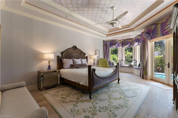 Bedroom with ceiling fan, a raised ceiling, light hardwood / wood-style flooring, and access to exterior
