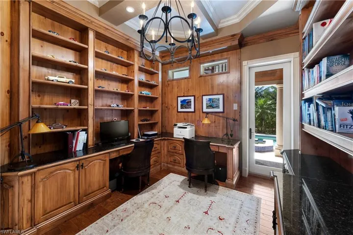 Office with built in desk, dark hardwood / wood-style flooring, crown molding, wood walls, and a notable chandelier