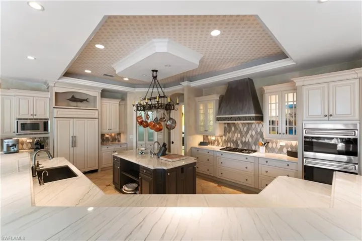 Kitchen featuring a kitchen island with sink, built in appliances, a tray ceiling, sink, and custom exhaust hood