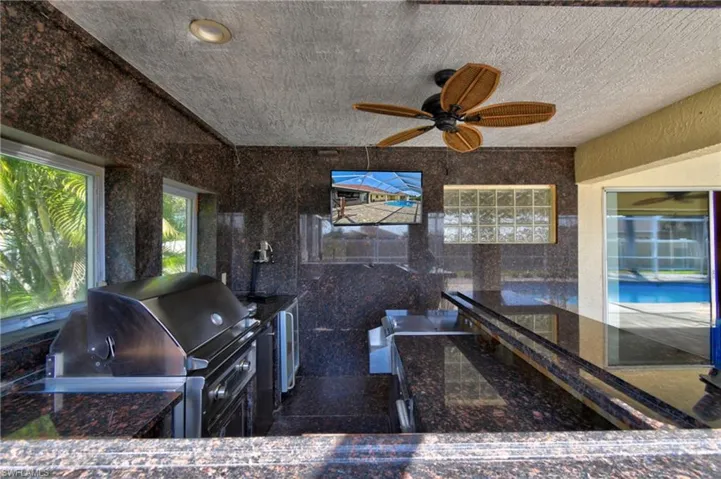 The full Summer kitchen, built entirely from granite, includes a grill, mini fridge, side burner, condiments organizer, wall-mounted TV, and roll-down electric hurricane shutters for your safety and more.
