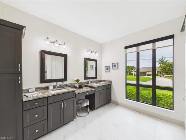Spacious bath featuring dual vanities with integrated sinks, ample dark cabinetry, and a large window with roller shades