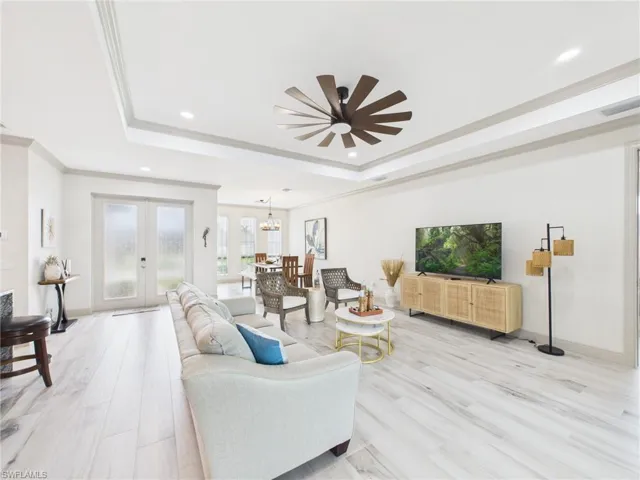 Spacious living area featuring light wood-finish flooring, a tray ceiling with recessed lighting, and a contemporary ceiling fan