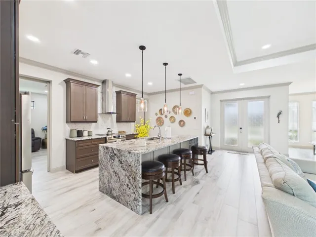 Open-concept kitchen featuring a large island with a waterfall countertop, pendant lighting, stainless steel appliances, and a tile backsplash