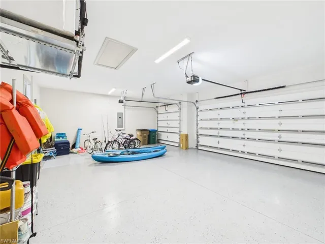 Spacious garage featuring a durable epoxy-coated floor, two overhead garage doors, ample overhead lighting, an exposed ceiling access panel, and a wall-mounted electrical panel