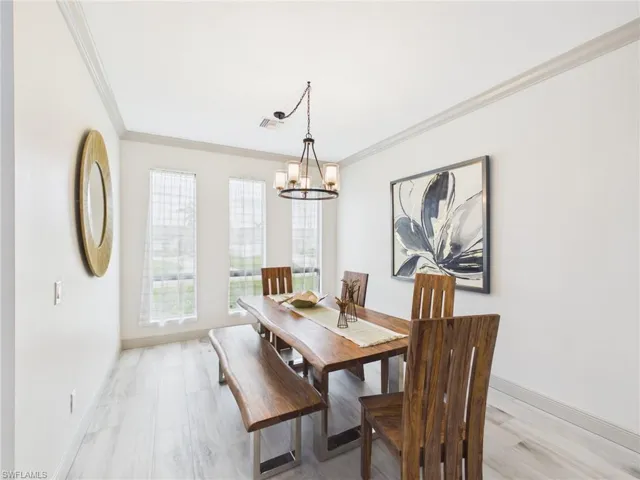 Bright dining area featuring light-toned wood-finish flooring, white walls with crown molding, and multiple tall windows