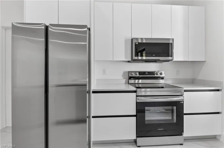 Kitchen featuring stainless steel appliances, white cabinetry, modern cabinets, light stone counters, and light marble finish flooring