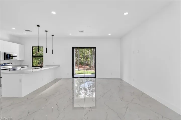 Kitchen with light marble finish floors, decorative light fixtures, stainless steel appliances, white cabinets, and light stone countertops