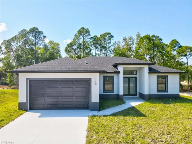 View of front of property with a front yard, concrete driveway, an attached garage, and stucco siding
