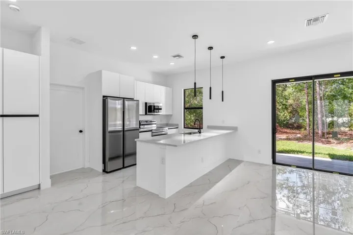 Kitchen with white cabinets, stainless steel appliances, hanging light fixtures, a peninsula, and light stone counters
