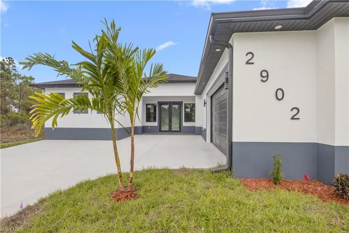 Entrance to property featuring french doors, stucco siding, a lawn, and driveway