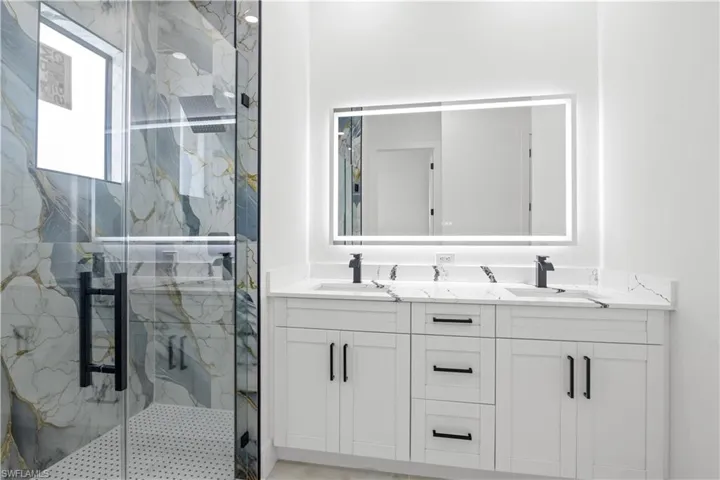 Full bath with double vanity and a marble finish shower