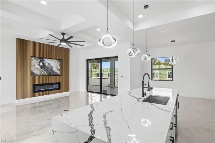 Kitchen featuring decorative light fixtures, healthy amount of natural light, light marble finish floors, light stone countertops, and coffered ceiling