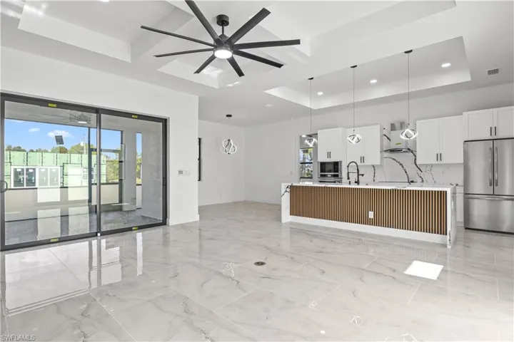 Kitchen with freestanding refrigerator, hanging light fixtures, white cabinets, light stone countertops, and a center island with sink