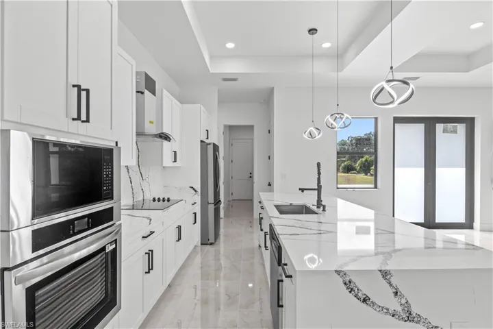 Kitchen featuring appliances with stainless steel finishes, light stone counters, decorative light fixtures, white cabinets, and recessed lighting