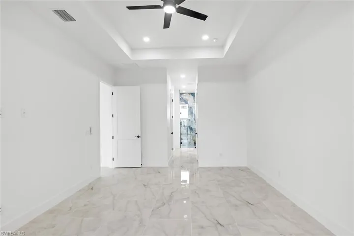 Unfurnished room featuring a raised ceiling, a ceiling fan, light marble finish flooring, and recessed lighting