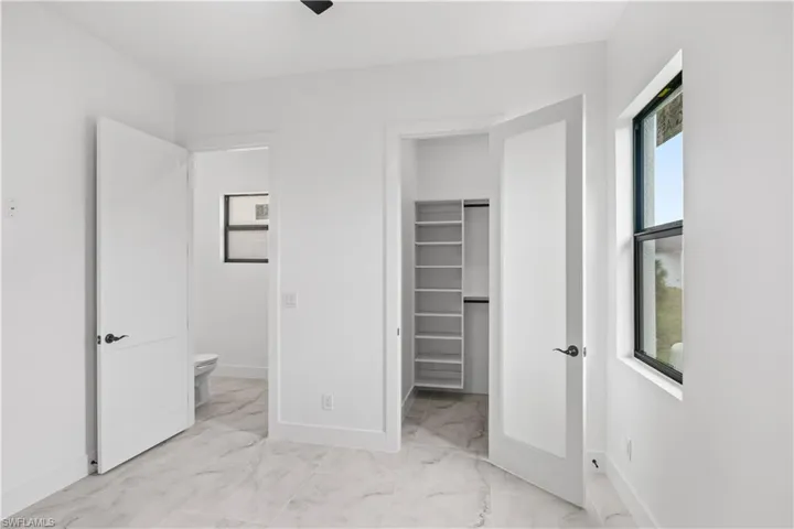 Unfurnished bedroom featuring a spacious closet, light marble finish flooring, and ceiling fan