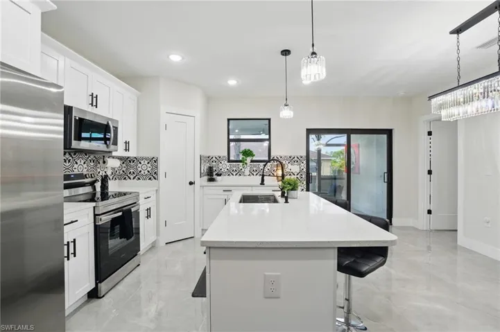 Kitchen with appliances with stainless steel finishes, a sink, decorative backsplash, light marble finish floors, and a kitchen island