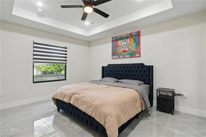 Bedroom featuring a tray ceiling, baseboards, recessed lighting, light marble finish floors, and ceiling fan