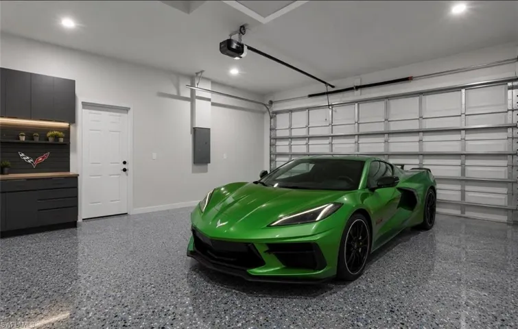 Garage featuring a speckled epoxy floor, built-in dark cabinetry with wood-finish countertops, overhead lighting, and an automated garage door