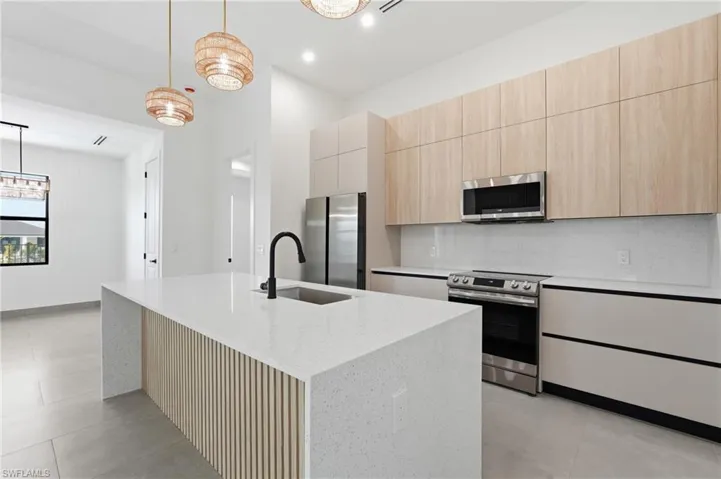 Modern kitchen featuring a large island with a waterfall countertop, integrated sink, and matte black faucet