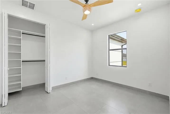 Room featuring light gray tile flooring, a window with dark framing, a built-in closet with shelving, a wooden ceiling fan, and recessed lighting