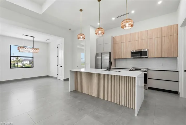 Modern kitchen featuring a waterfall island with wood-finish slat detailing, quartz countertops, stainless steel appliances, and light wood-finish upper cabinetry