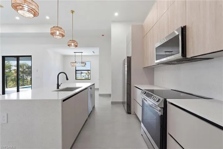 Modern kitchen featuring light wood-finish cabinetry, stainless steel appliances, and a central island with a waterfall-edge countertop