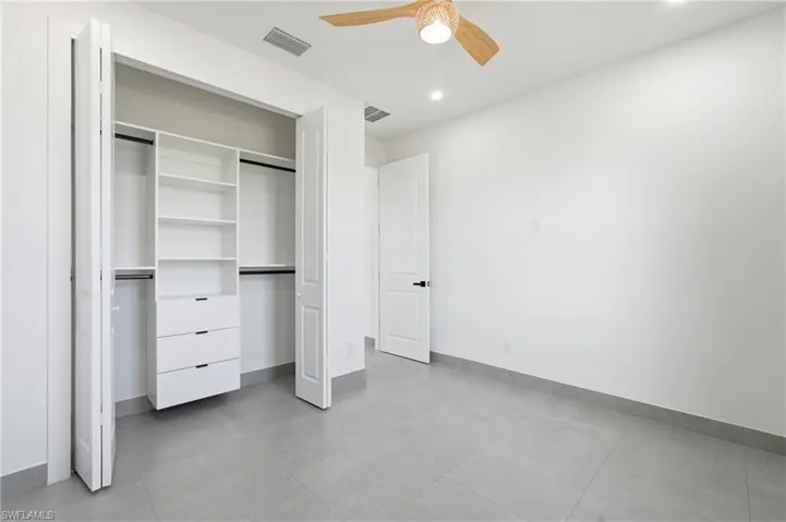 Bedroom featuring a built-in closet system with shelving and drawers, white walls, gray tile flooring, and a ceiling fan with a natural wood finish