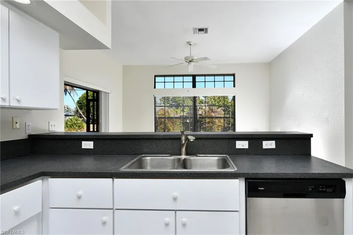 Kitchen featuring dark countertops, dishwasher, white cabinets, and healthy amount of natural light