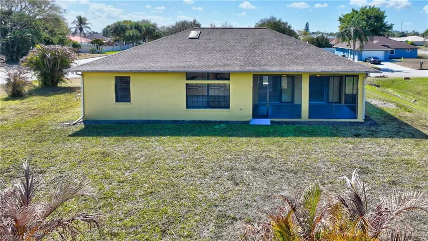 Back of property featuring a yard, stucco siding, roof with shingles, and a sunroom