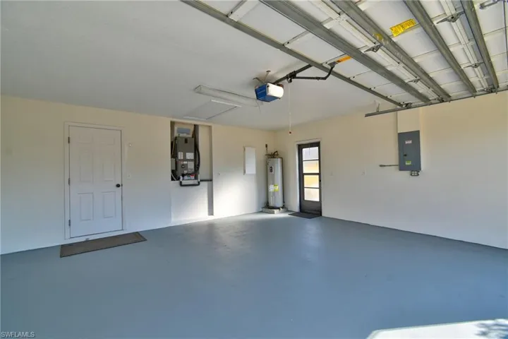Garage featuring electric panel, electric water heater, heating unit, and a garage door opener