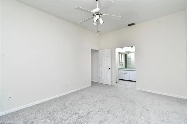 Unfurnished bedroom featuring light carpet, a ceiling fan, ensuite bath, and a high ceiling