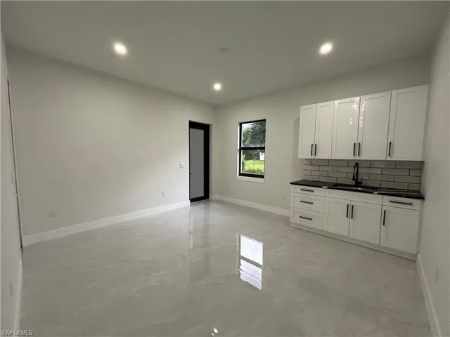 Kitchen featuring backsplash, dark countertops, recessed lighting, concrete floors, and white cabinets