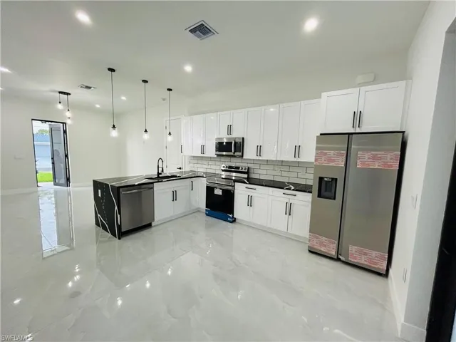 Kitchen with appliances with stainless steel finishes, backsplash, dark countertops, white cabinets, and recessed lighting