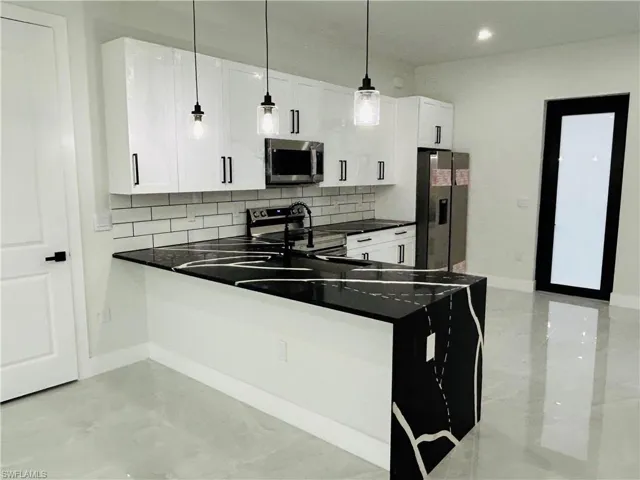 Kitchen with appliances with stainless steel finishes, dark countertops, decorative backsplash, decorative light fixtures, and recessed lighting