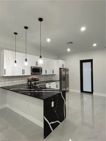 Kitchen featuring fridge, dark countertops, a peninsula, tasteful backsplash, and recessed lighting
