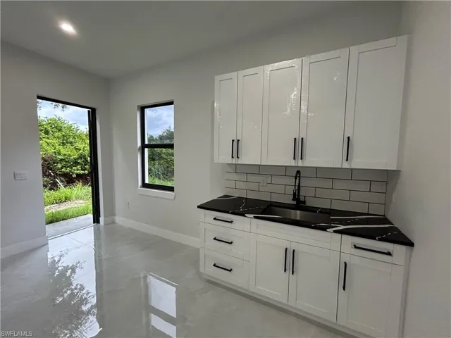 Kitchen featuring decorative backsplash, dark countertops, light marble finish flooring, white cabinets, and recessed lighting