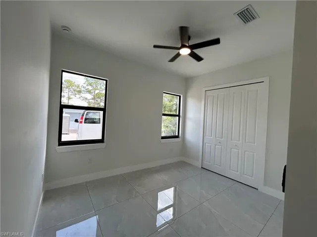 Unfurnished bedroom with light marble finish flooring, baseboards, a closet, and ceiling fan